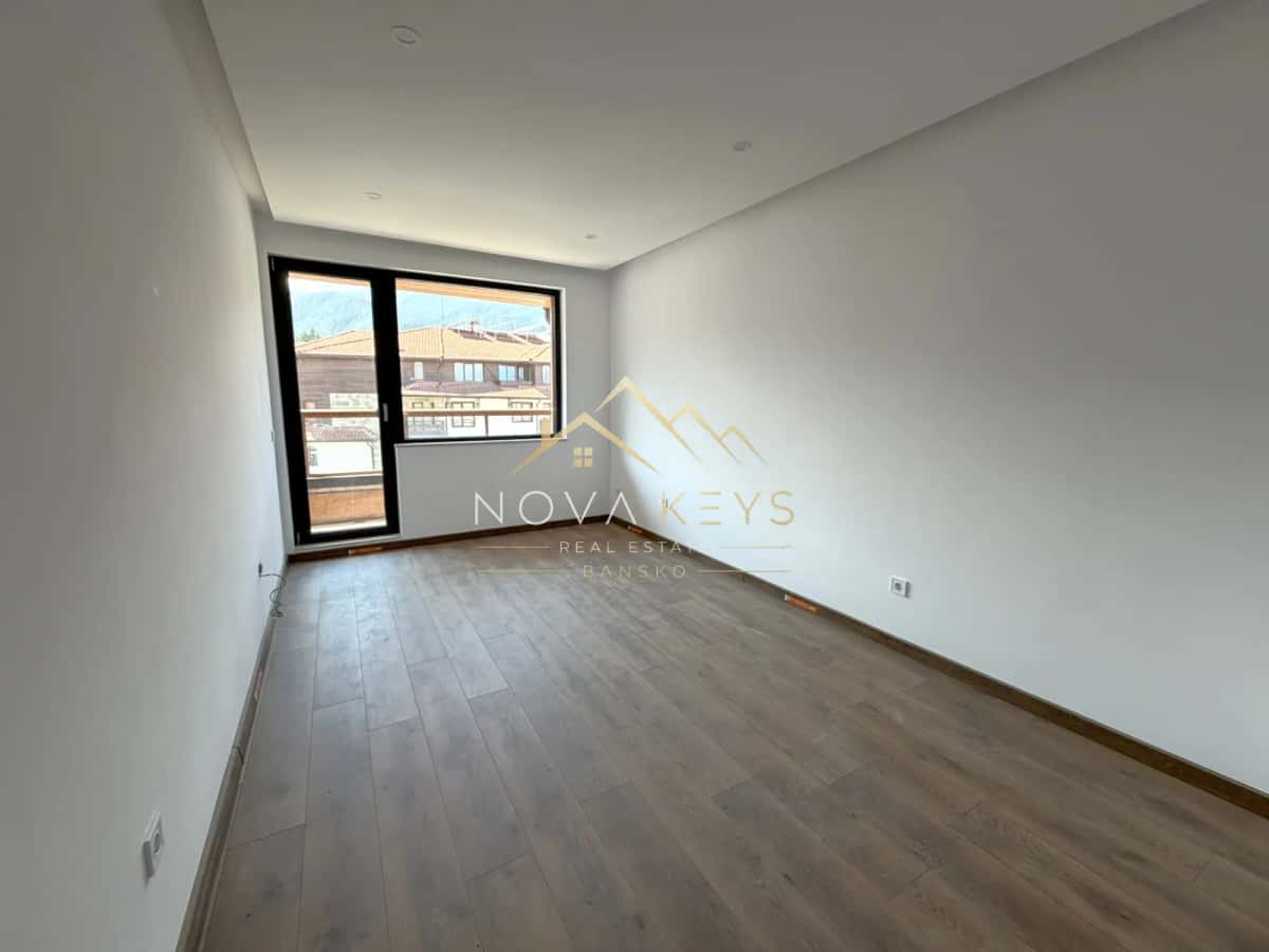 empty room with large window and wood flooring, two-bedroom apartment for sale in the Bansko ski area.