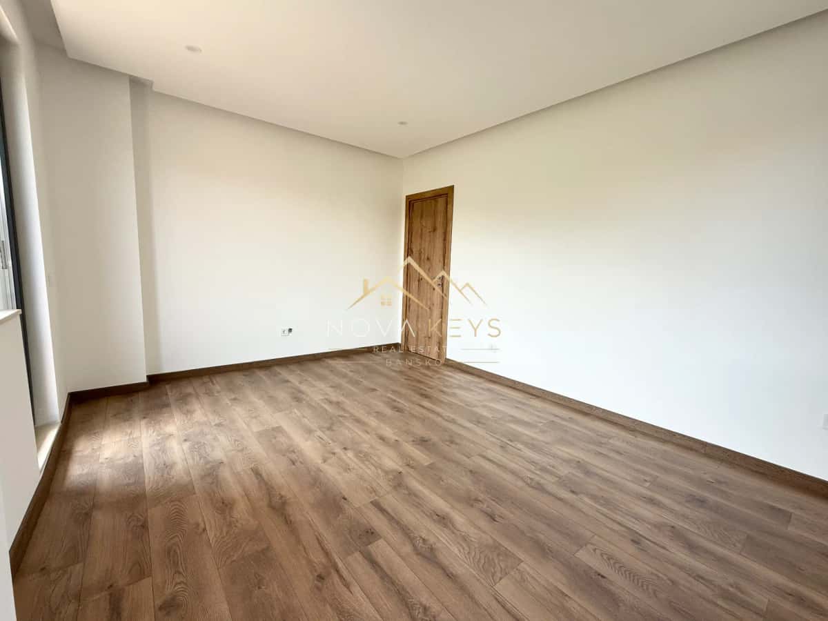 Empty room with wood flooring and wooden door, three-bedroom apartment for sale in the Bansko ski area.
