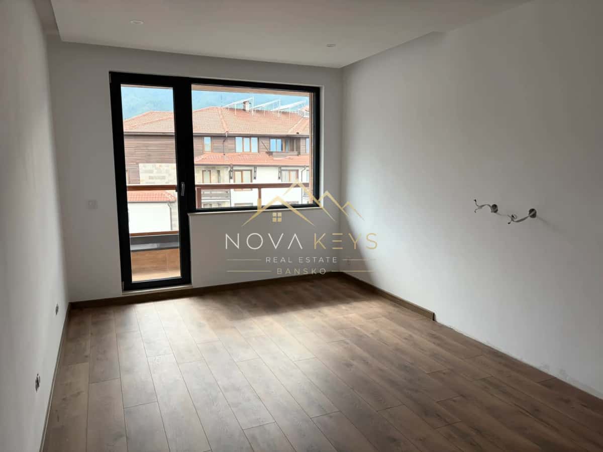 Empty room with wood-look flooring and large window, two-bedroom apartment for sale in the Bansko ski area.