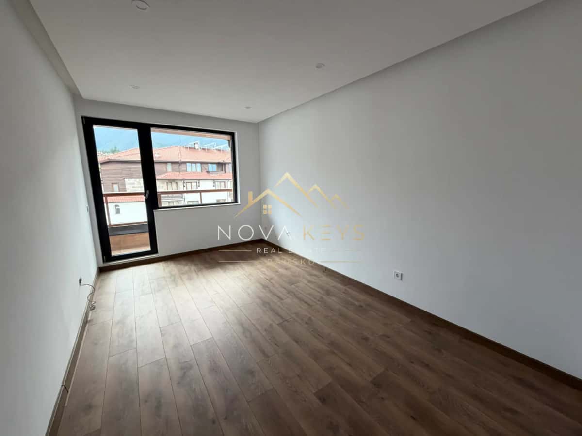 Empty room with wood flooring and balcony door, two-bedroom apartment for sale in the Bansko ski area.