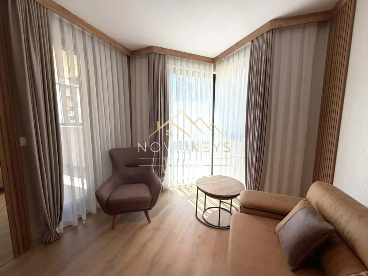 small sitting room with armchair, sofa, and round coffee table, two-bedroom apartment for sale in the Bansko ski area.