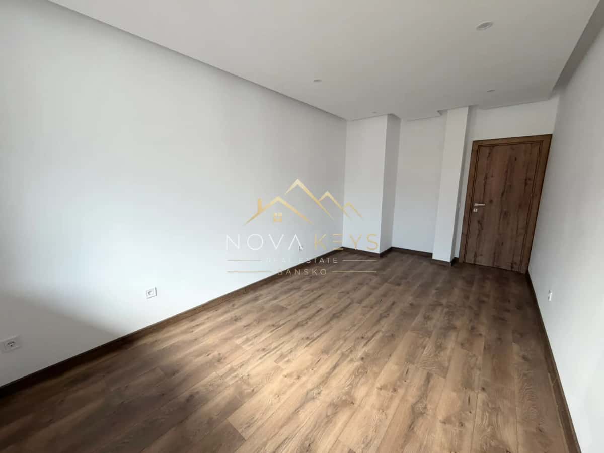 Empty room with wood-look flooring and wooden door, two-bedroom apartment for sale in the Bansko ski area.