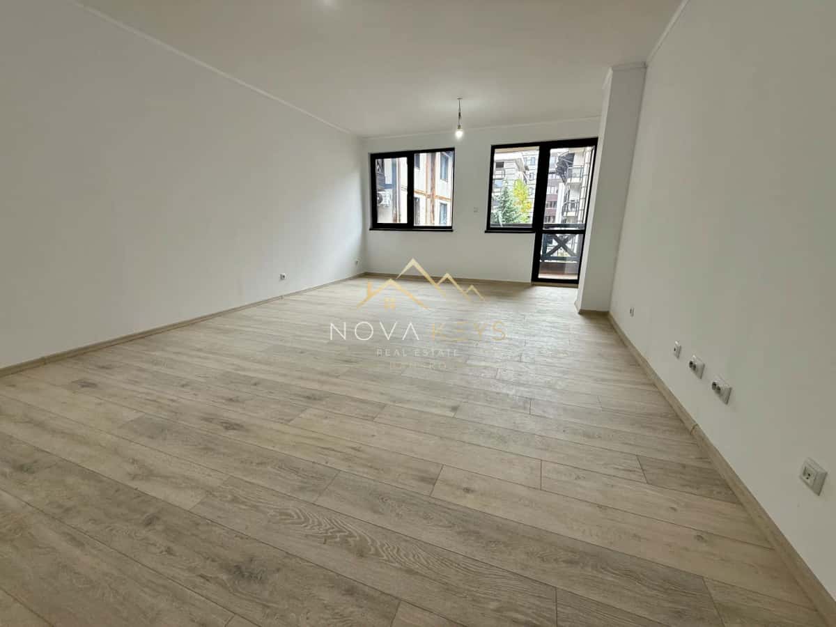 Empty room with wood flooring and windows, two-bedroom apartment for sale in Bansko centre.