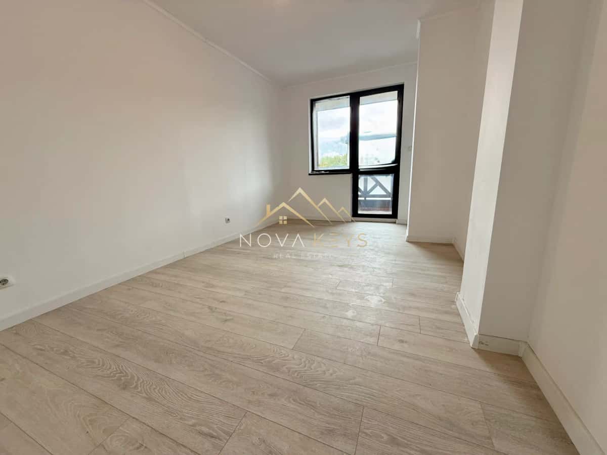 Empty room with light wood floor and black-framed window, two-bedroom apartment for sale in Bansko.