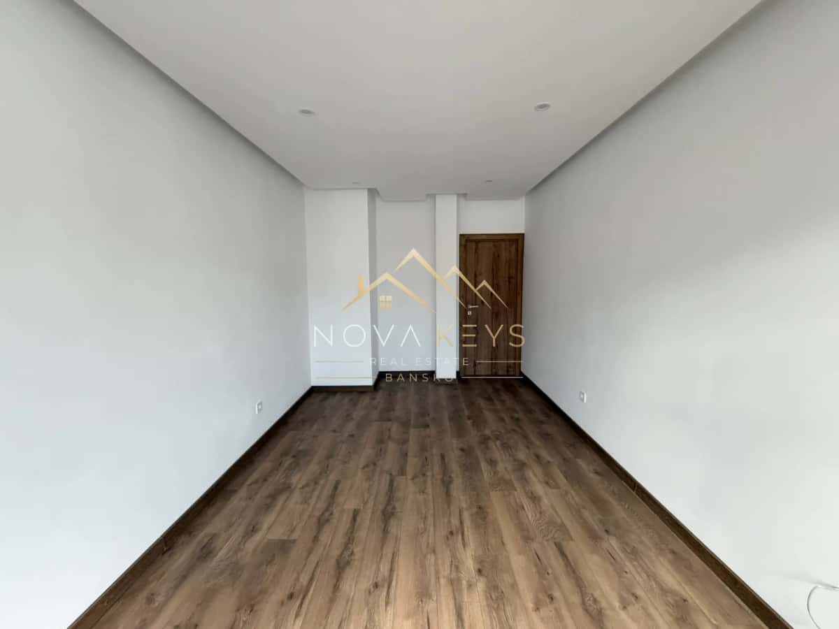 empty narrow room with wood-look flooring and wooden door, two-bedroom apartment for sale in the Bansko ski area.