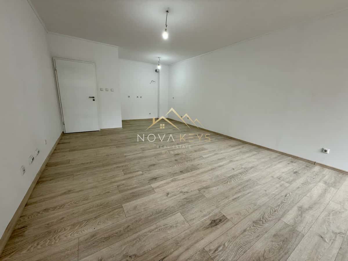 Empty room with wood-look flooring and white walls, two-bedroom apartment for sale in Bansko centre.