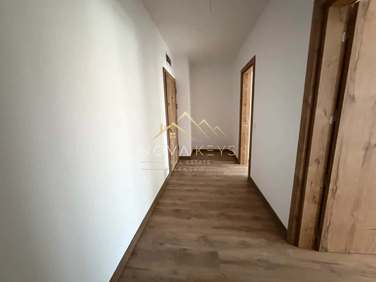 Narrow hallway with wood-look flooring and wooden doors, two-bedroom apartment for sale in the Bansko ski area.