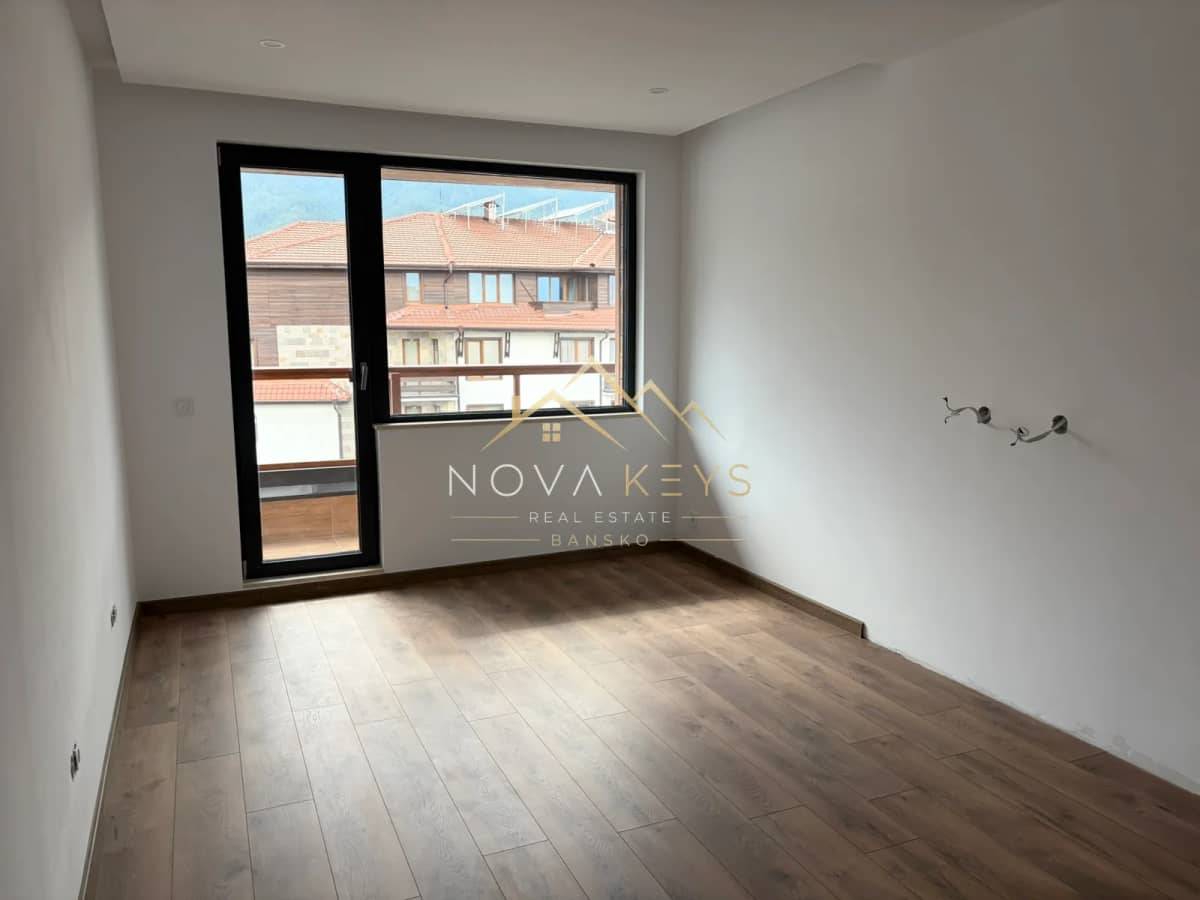 Empty room with wood-look flooring and large window, two-bedroom apartment for sale in the Bansko ski area.