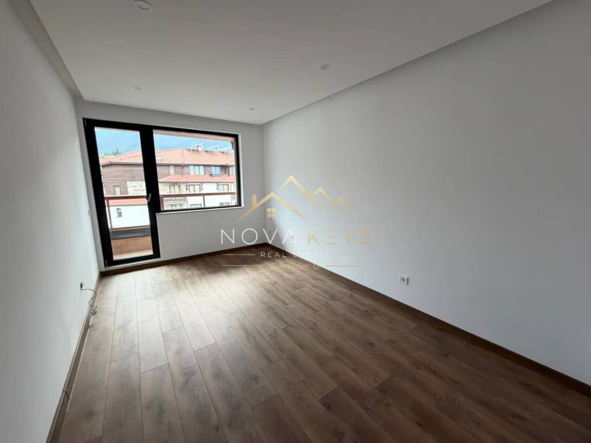 Empty room with wood flooring and balcony door, two-bedroom apartment for sale in the Bansko ski area.