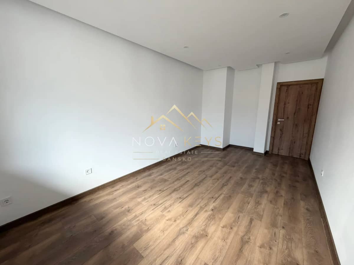Empty room with wood-look flooring and wooden door, two-bedroom apartment for sale in the Bansko ski area.