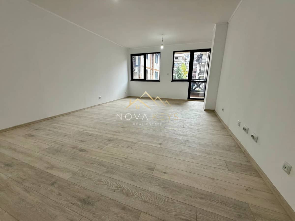 Empty room with wood flooring and windows, two-bedroom apartment for sale in Bansko centre.
