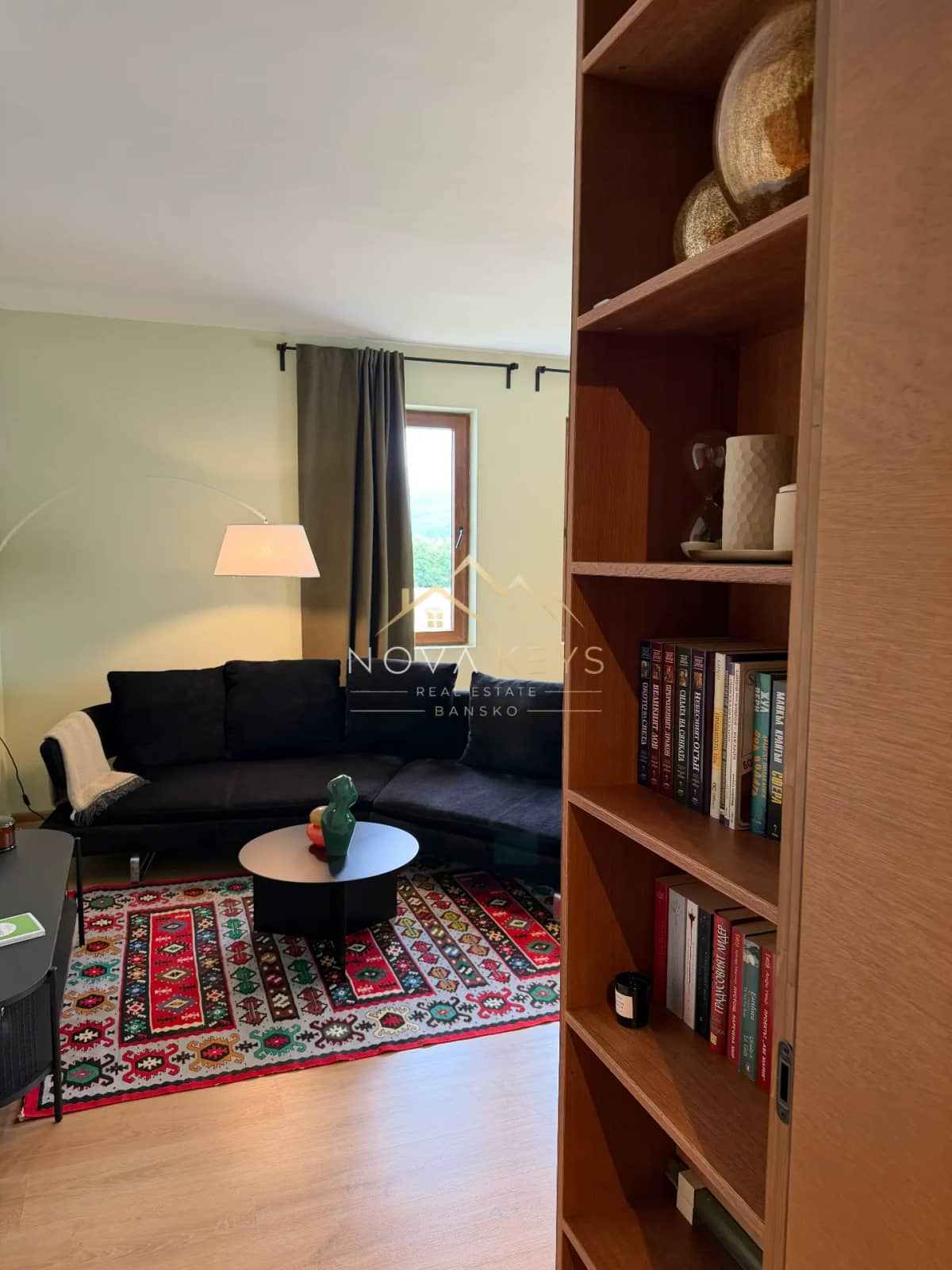 Living room with black sofa and bookshelf, two-bedroom apartment for sale in Pirin Golf.