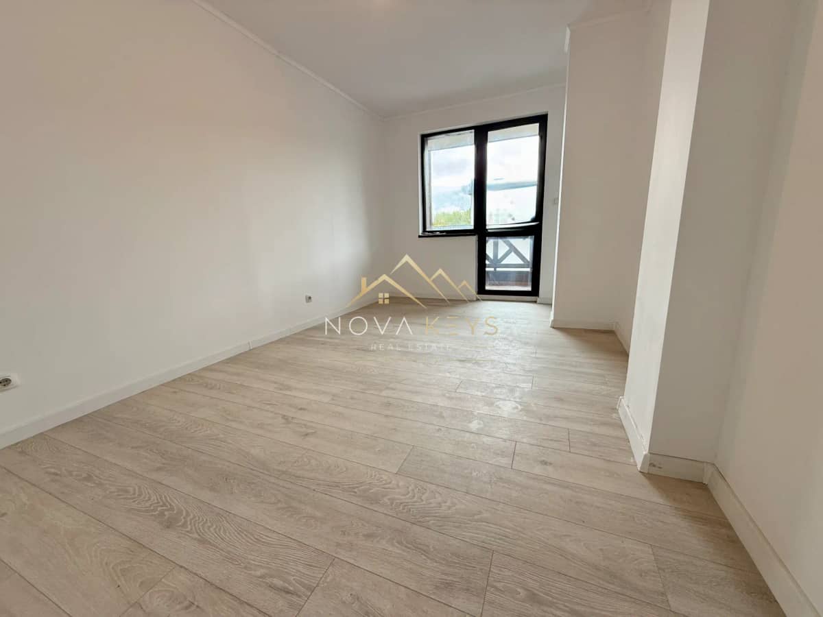 Empty room with light wood floor and black-framed window, two-bedroom apartment for sale in Bansko.