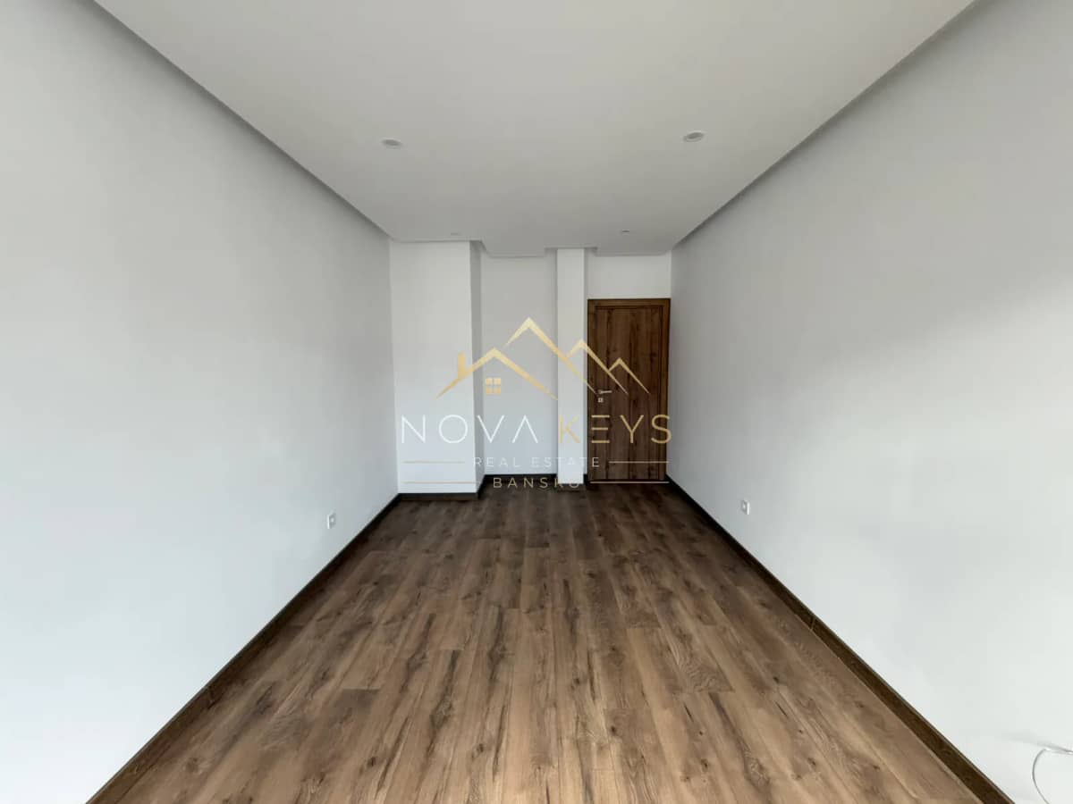 empty narrow room with wood-look flooring and wooden door, two-bedroom apartment for sale in the Bansko ski area.