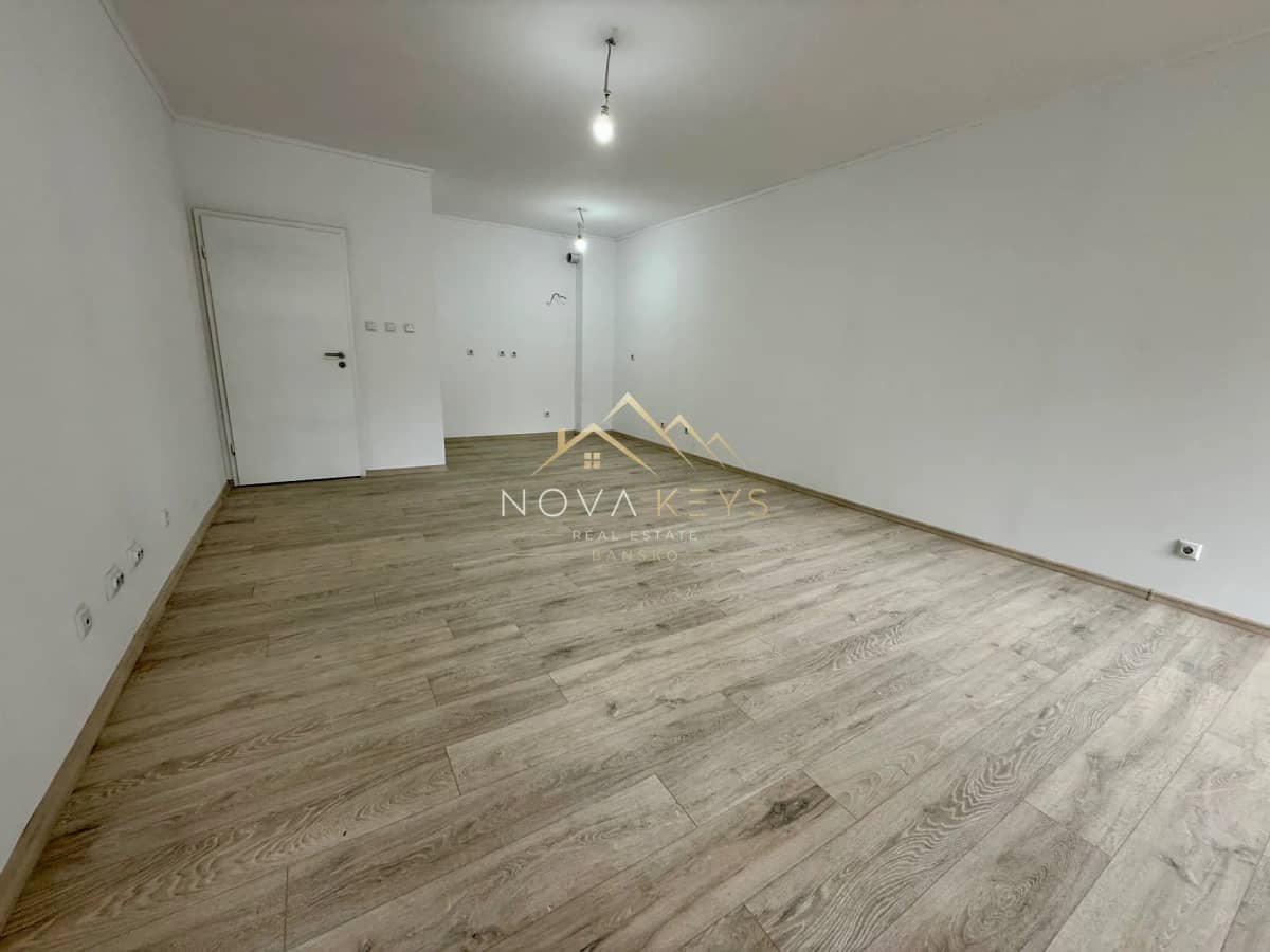 Empty room with wood-look flooring and white walls, two-bedroom apartment for sale in Bansko centre.