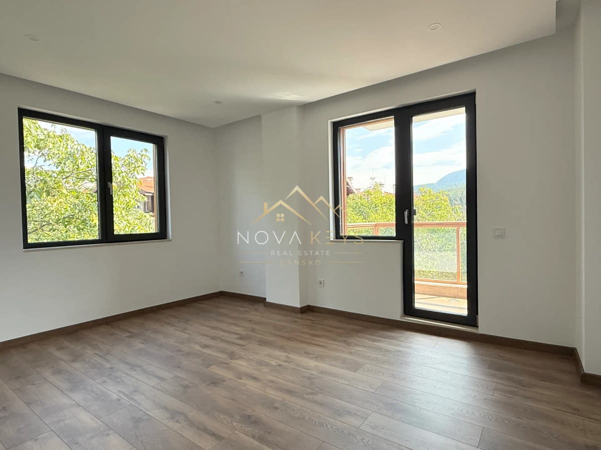 Empty room with wood flooring and black-framed windows, three-bedroom apartment for sale in the Bansko ski area.