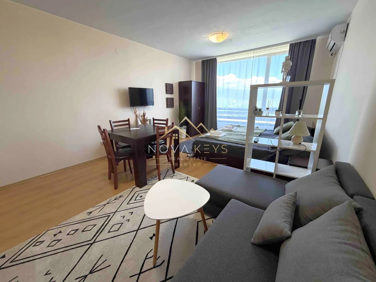 Living room with sofa, dining table, and large window, studio for rent in Razlog.