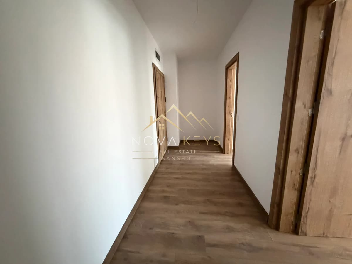 Narrow hallway with wood-look flooring and wooden doors, two-bedroom apartment for sale in the Bansko ski area.